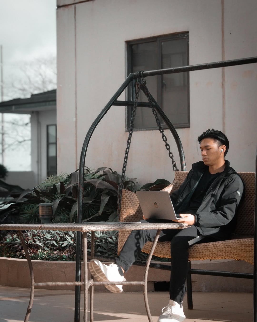 Elcid Villegas working on a laptop on an outdoor porch swing.
